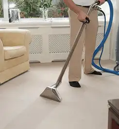 Professional carpet cleaner using a hot-water extraction wand and hose machine in a living room in Cleveland, OH.